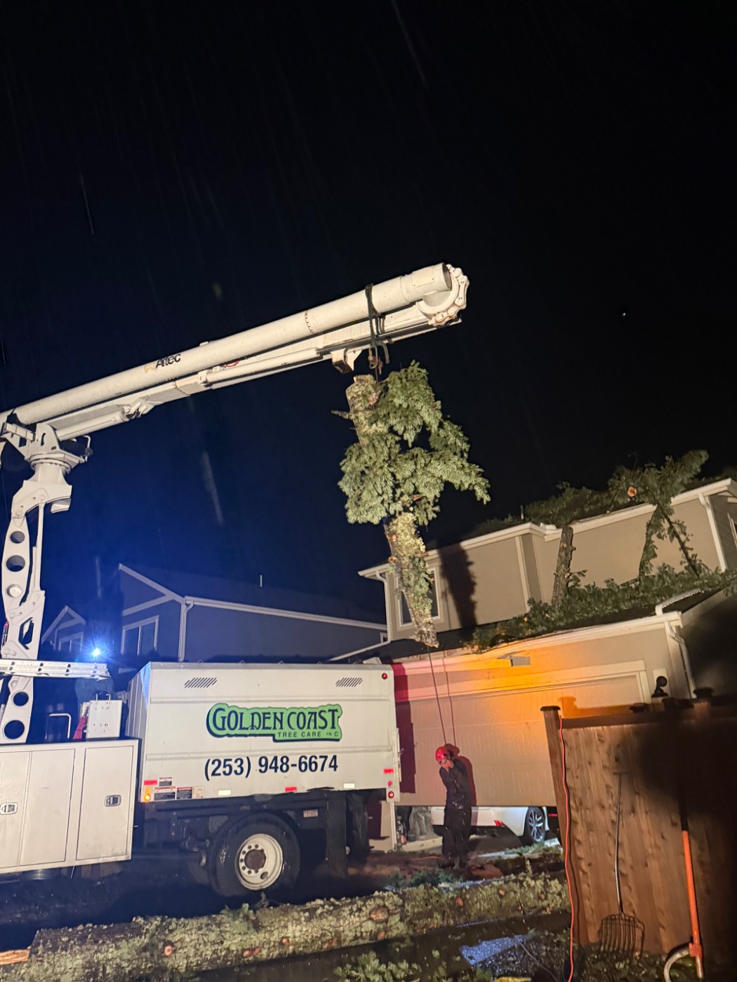 Golden Coast Tree Care crane truck removing a fallen tree from a house at night in the rain