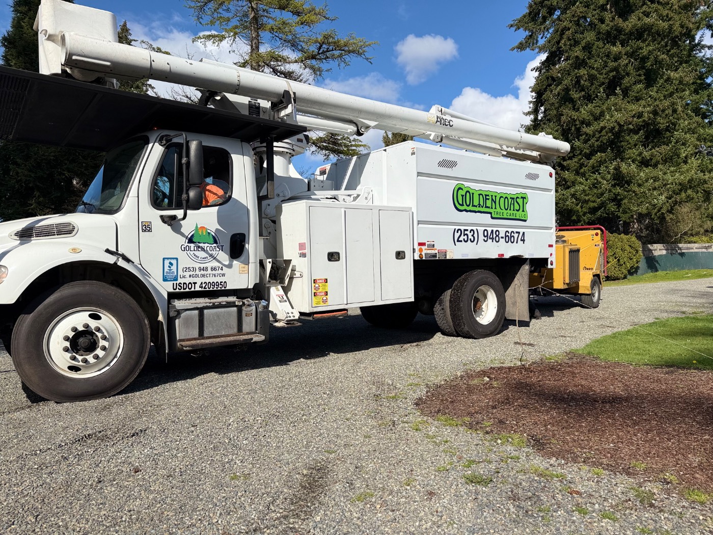 Golden Coast Tree Care bucket truck and chipper on a clear job site